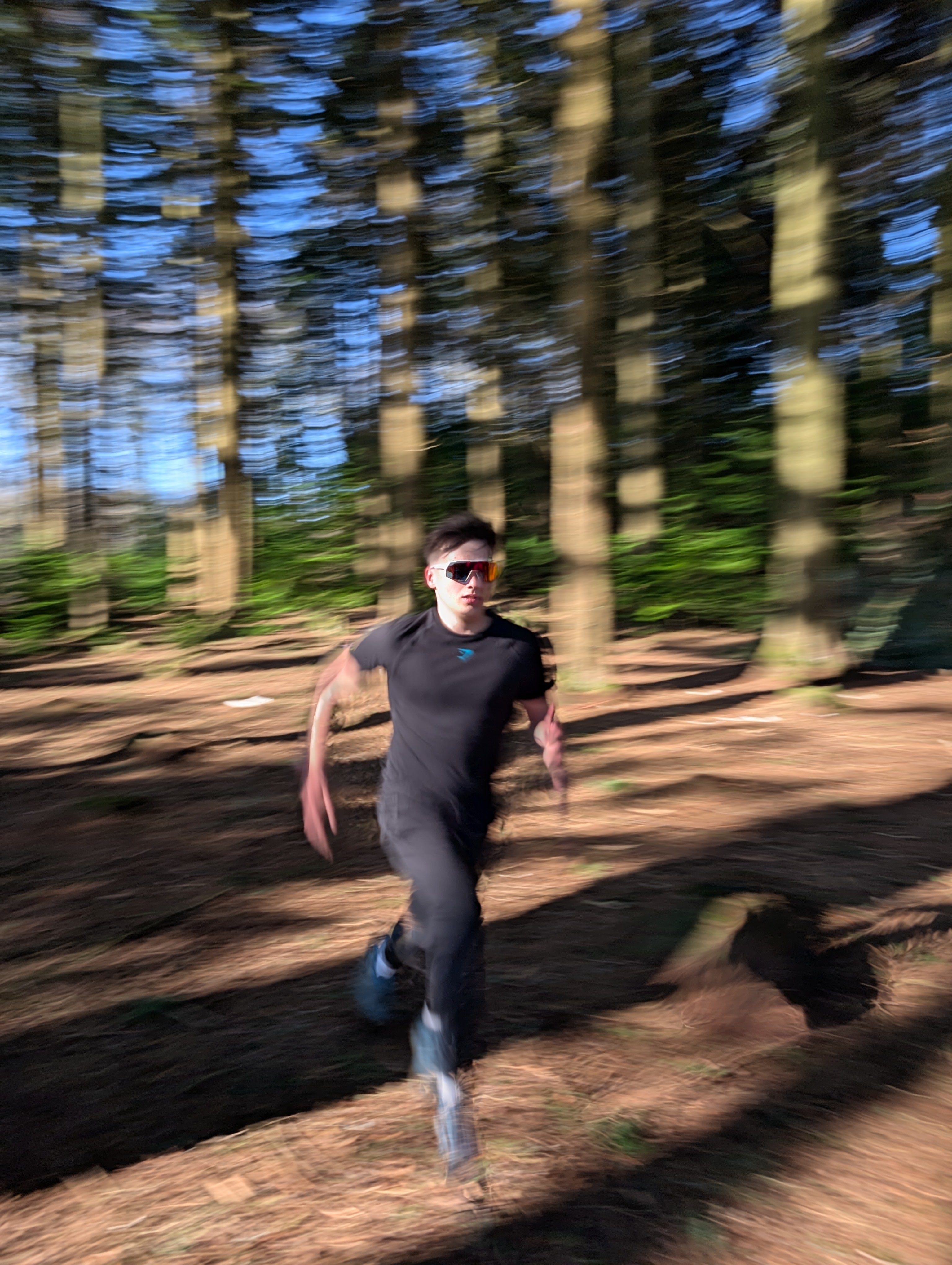 A man running fast through woodland wearing sports glasses
